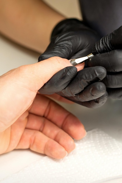 Cierre al maestro manicurista profesional sosteniendo la mano del cliente mientras usa un empujador de cutículas en un salón de uñas
