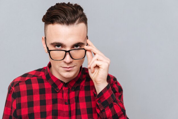 Foto cierre para arriba hipster guapo en camisa roja sosteniendo sus gafas. fondo gris aislado