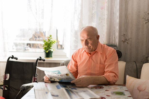 Cierre para arriba sentado feliz senior hombre leyendo artículos del periódico blanco relajante en la sala de estar.