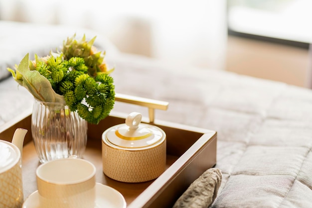 Cierre la bandeja de té de madera y la decoración de un jarrón de flores de cristal en una cama blanca y suave en el dormitorio con una suave luz solar por las vacaciones de fin de semana por la mañana