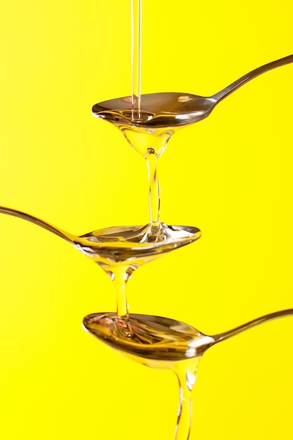 Cierre las cucharas en las que se vierte miel líquida sobre un fondo amarillo