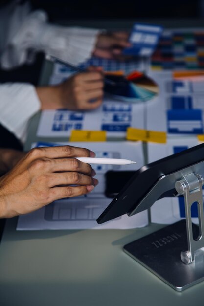 Cierre el desarrollador de ux y el diseñador de ui intercambiando ideas sobre el diseño de estructura alámbrica de la interfaz de la aplicación móvil en la mesa con el resumen del cliente y el código de color en la oficina modernaAgencia de desarrollo digital creativa