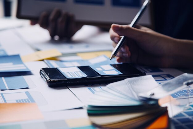 Cierre el desarrollador de ux y el diseñador de ui intercambiando ideas sobre el diseño de estructura alámbrica de la interfaz de la aplicación móvil en la mesa con el resumen del cliente y el código de color en la oficina modernaAgencia de desarrollo digital creativa