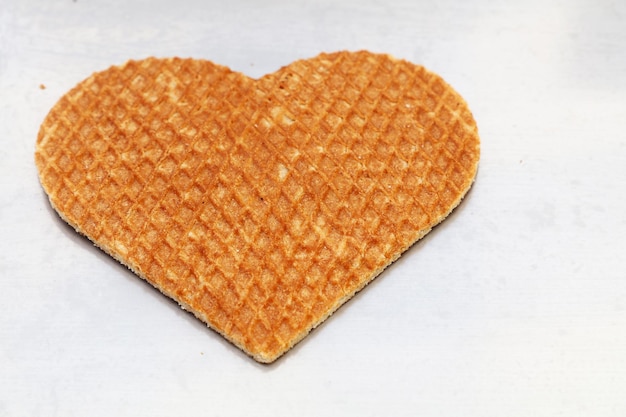 Cierre una galleta dulce tradicional holandesa stroopwafel (waffle de jarabe) en forma de corazón en papel de hornear blanco, vista de ángulo alto