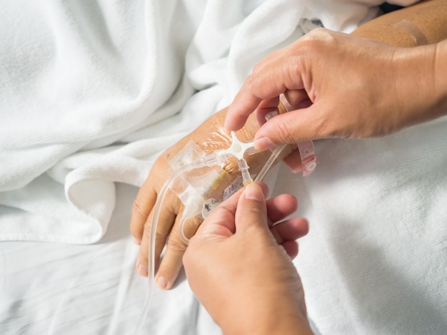Foto cierre de la mano de la enfermera, ajuste de tres vías del conjunto iv para el goteo de solución salina por goteo intravenoso fluido en blanco