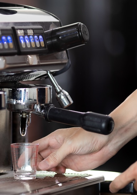 Cierre de la mano de hacer café con la máquina en la cafetería. La máquina de café espresso moderna profesional vierte bebida caliente en la taza. Concepto de café en la cafetería.