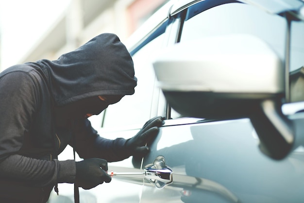 Cierre la mano de un ladrón de autos sosteniendo un destornillador y un guante negro robando un automóvil tratando de manejar la puerta para ver si el vehículo está desbloqueado tratando de entrar al interior