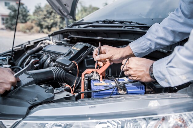 Cierre la mano del mecánico de automóviles usando la medición de comprobación de la batería del coche.