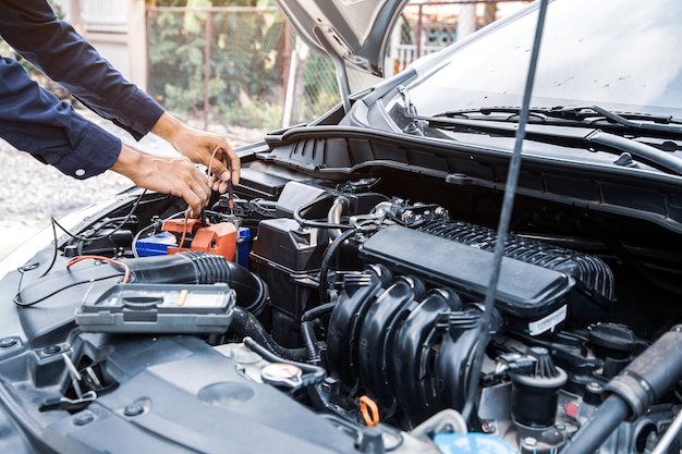 Cierre la mano del mecánico de automóviles usando la medición de comprobación de la batería del coche.