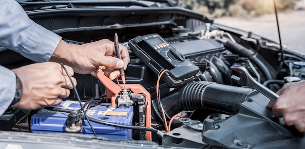 Cierre la mano del mecánico de automóviles usando la medición de comprobación de la batería del coche.