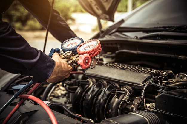 Cierre la mano del mecánico usando acondicionadores de aire de automóviles de llenado de manómetro múltiple.