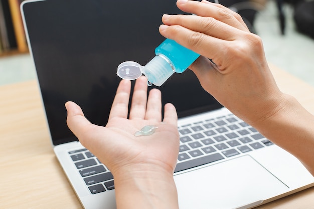 Cierre la mano usando gel desinfectante para la prevención de coronavirus de higiene de manos antes de trabajar con la computadora portátil en casa.