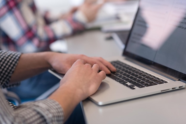 cierre de las manos de un hombre de negocios escribiendo en una computadora portátil en una oficina de inicio moderna, equipo borroso en la reunión, grupo de personas en segundo plano