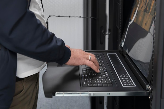 Cierre las manos del ingeniero del centro de datos usando el teclado en una supercomputadora. Instalación especializada en salas de servidores con un administrador de sistemas masculino que trabaja con la red de protección de datos para la seguridad cibernética.