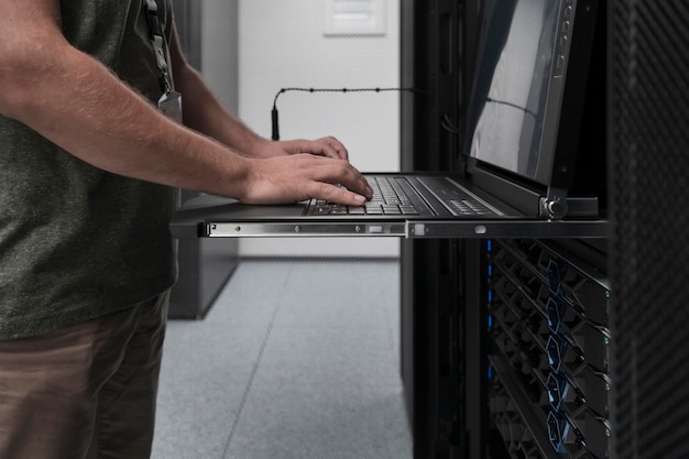 Foto cierre las manos del ingeniero del centro de datos usando el teclado en una supercomputadora. instalación especializada en salas de servidores con un administrador de sistemas masculino que trabaja con la red de protección de datos para la seguridad cibernética.