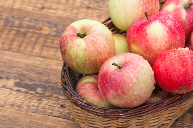 Cierre las manzanas rojas en la cesta de mimbre sobre tablas de madera antiguas.