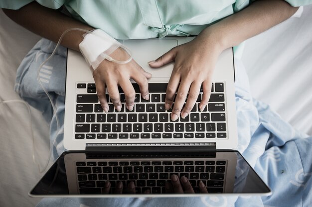 El cierre de la mujer enferma trabaja con la computadora portátil en hospital.