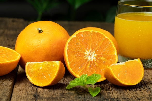 Cierre la naranja cortada por la mitad con rodajas de naranja y un vaso de jugo de naranja en la mesa de madera.