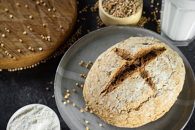 Cierre el pan de trigo sarraceno verde y la leche de trigo sarraceno orgánica. Plato de cerámica gris hecho en casa, servilleta de lino. Horneado saludable inofensivo, saludable y sin gluten para veganos. Pan alternativo y leche vegetal