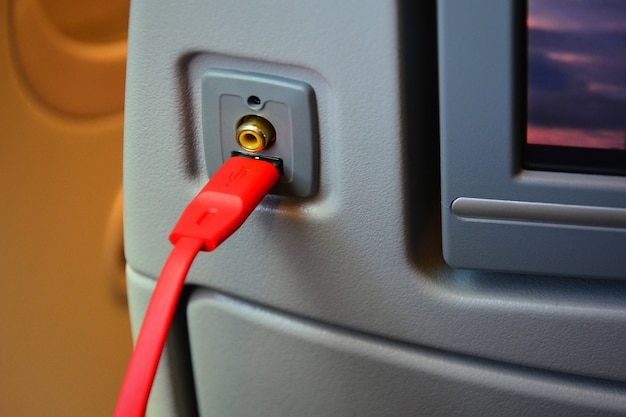 Foto cierre el puerto aux y el cargador del enchufe usb con el cable usb rojo en la parte trasera del asiento del avión