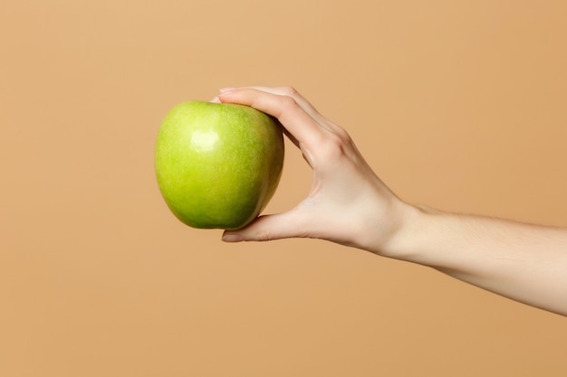 Cierre recortado de hembra sostiene en la mano fruta fresca de manzana verde madura aislada en la pared de color beige pastel