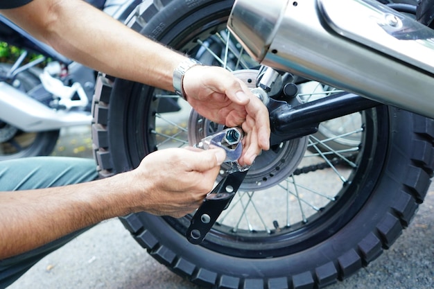 Cierre la rueda de la motocicleta fijada a mano del trabajador técnico en el exterior del garaje