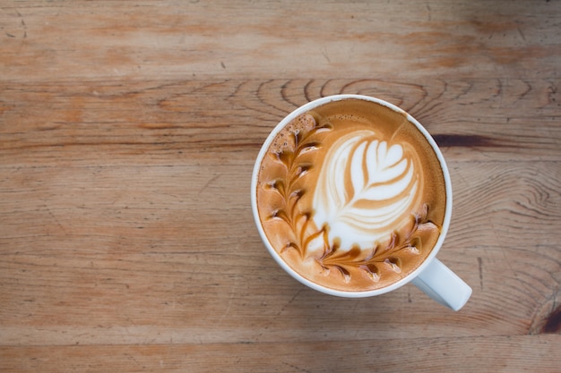 Cierre de la taza de café caliente del arte del latte en la tabla de madera.