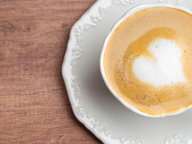 Cierre de la taza de café con leche con forma de corazón arte de latte en la mesa de madera en el café