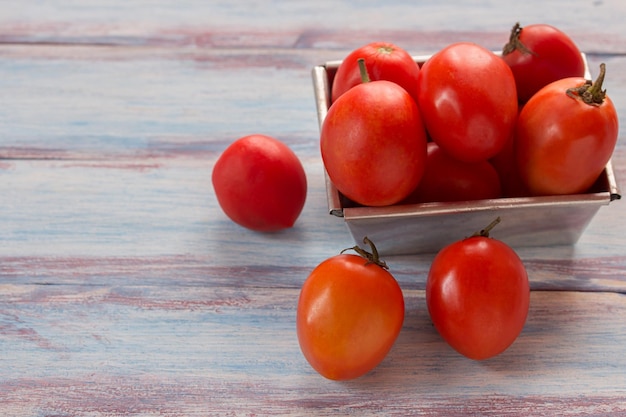 Cierre los tomates de ciruela roja en un recipiente de acero inoxidable sobre el fondo de la mesa de madera
