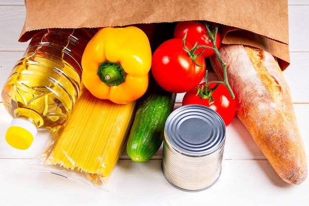 Cierre varios alimentos saludables, tomate, pan, pasta en una bolsa de papel sobre fondo blanco. Concepto de entrega de alimentos.