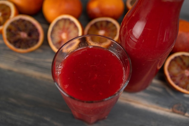 Cierre un vaso de jugo de naranja sanguina con fruta a la mitad en una mesa de madera