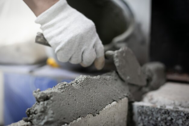 Ciérrese para arriba del albañil industrial que instala ladrillos en el emplazamiento de la obra, construyendo las paredes.