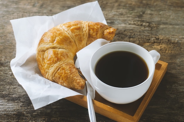 Ciérrese para arriba de café sólo con el cruasán en la tabla de madera con tono del vintage y de la ilustración