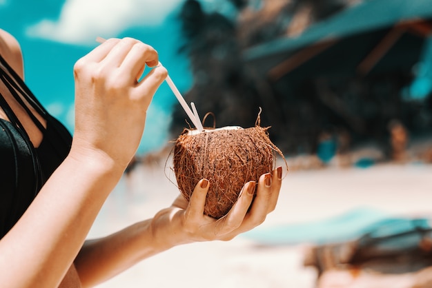 Ciérrese para arriba del cóctel de consumición de la muchacha en coco mientras que se coloca en la playa.