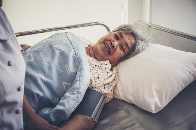 Ciérrese para arriba de la enfermera joven se ocupa de los pacientes mayores que miden la presión durante admitir en hospital.