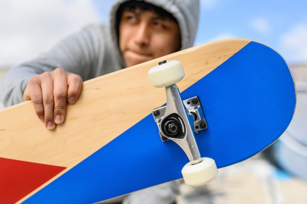 Ciérrese para arriba del hombre joven que sostiene longboard o el monopatín en el parque.