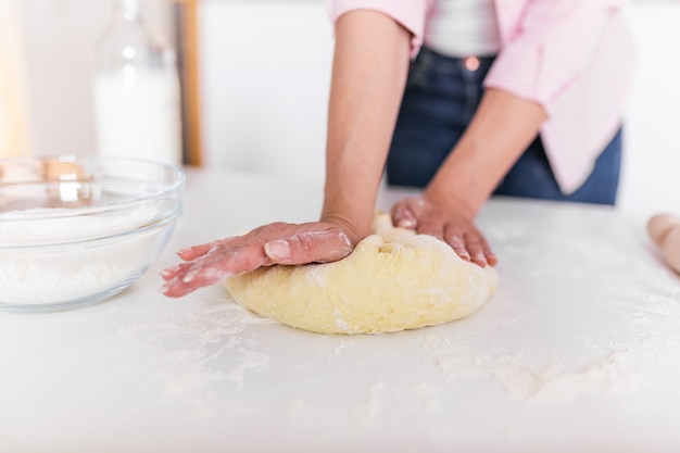 Ciérrese para arriba de las manos femeninas del panadero que amasan la masa y que hacen el pan.