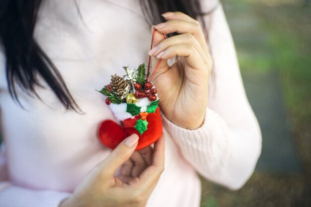 Ciérrese para arriba de las manos femeninas que sostienen las decoraciones, la bota y la cinta de una Navidad.