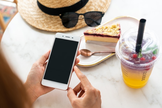 Ciérrese para arriba de las manos de las mujeres que sostienen el teléfono móvil en café.