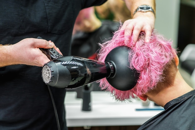 Ciérrese para arriba de las manos de los peluqueros que secan el pelo rosado corto con el secador de pelo.