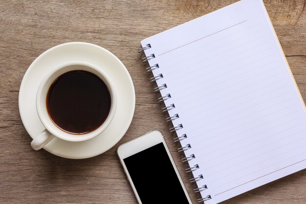 Ciérrese para arriba de la mesa de madera vieja con el cuaderno, el smartphone y la taza de café.