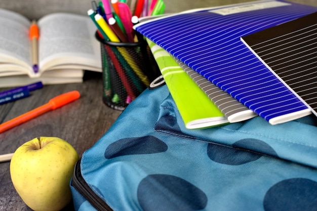 Ciérrese para arriba de una mochila, fuentes de escuela en un fondo de madera.