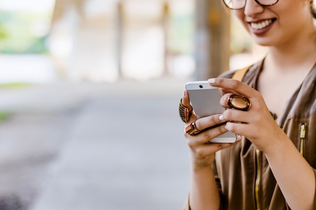 Ciérrese para arriba de muchacha sonriente feliz con el teléfono móvil, escribiendo el mensaje afuera en la calle.