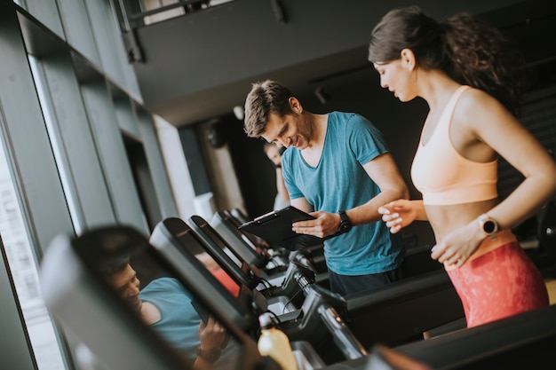 Ciérrese para arriba de mujer con el instructor que se resuelve en la rueda de ardilla en gimnasio