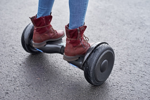 Ciérrese para arriba de la mujer que usa hoverboard en la carretera de asfalto. Pies en scooter eléctrico al aire libre