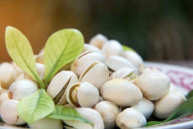 Ciérrese para arriba de las nueces de pistachos en la tabla de madera. Pistacho en cuenco de madera con hojas verdes