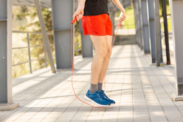 Ciérrese para arriba de las piernas masculinas que saltan con la comba al aire libre. Ejercicio y estilo de vida.