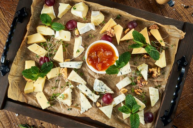 Ciérrese para arriba en la placa de queso servida con las nueces, las uvas, la miel. Vista desde arriba sobre diferentes tipos de queso en la superficie oscura con espacio de copia. quesos variados