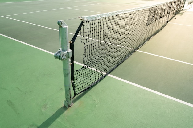 Ciérrese para arriba de una red en un campo de tenis duro en un día soleado.