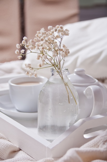 Ciérrese para arriba de la taza de té, de leche, de tetera y de ramo de flores blancas en la bandeja blanca.